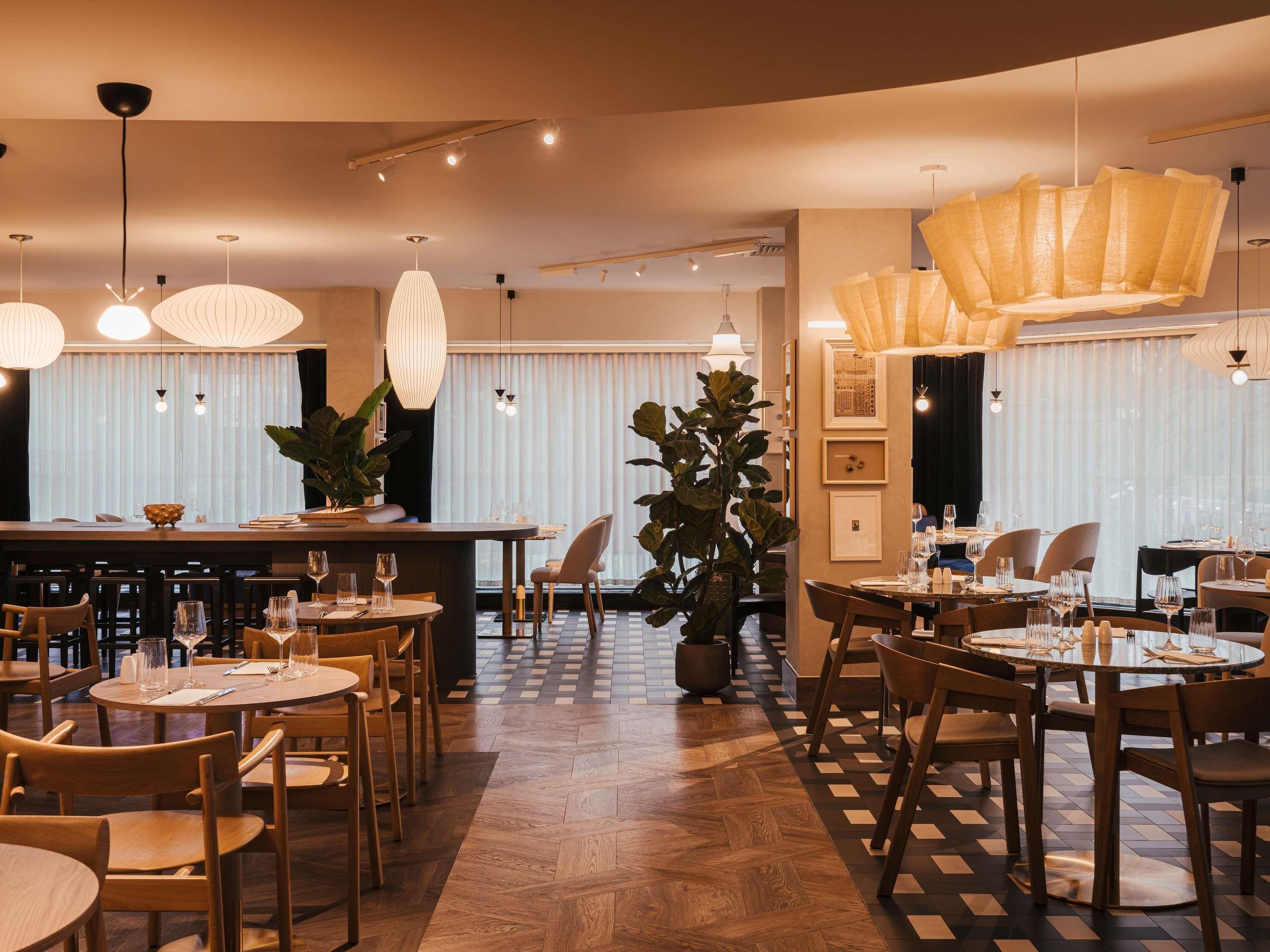En restaurant med flere spiseborde og stole, et barområde og hængende pendellamper.