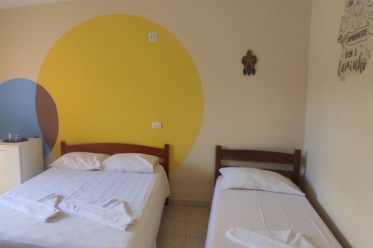 Une chambre avec deux lits simples, un petit bureau avec une chaise et un mur orné d’un grand cercle jaune.