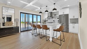 A modern kitchen with a large island, bar stools, and a view to the outside.