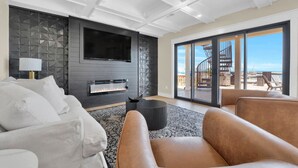 A modern living room with a fireplace, a large TV, and a view of the outside balcony.
