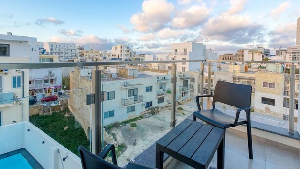 Un balcón con vistas a una zona residencial, una piscina y una mesa de comedor con sillas.