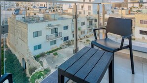 Un balcón con dos sillas y una mesa, con vistas a una zona residencial de edificios modernos y un cielo despejado.