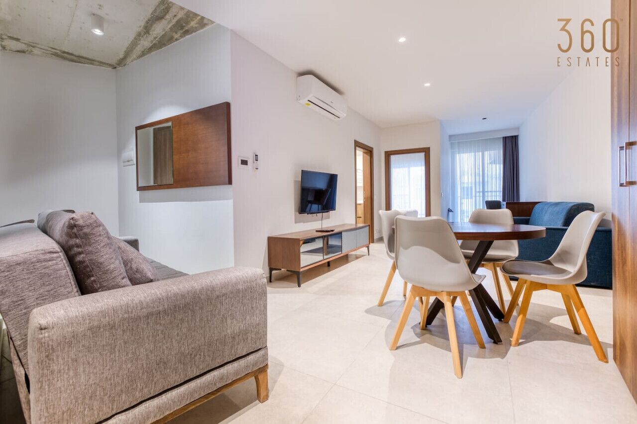 Una sala de estar moderna con sofá, mesa de comedor, sillas, televisor y aire acondicionado.
