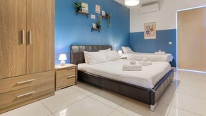 A bedroom with a large bed, a wardrobe, a bedside table with a lamp, and a wall-mounted shelf with plants. - Designer, fully equipped 3BR home in Gzira w/WIFI (Il-Gżira)