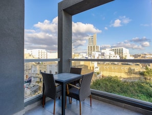 A balcony with a table and chairs, offering a view of surrounding buildings and a clear sky. - Designer, fully equipped 3BR home in Gzira w/WIFI (Il-Gżira)