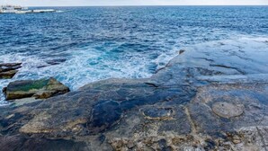 Una costa rocosa amb aigua blava i cristal·lina i un vaixell a la distància.
