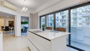 A modern apartment with a large kitchen island, a dining area, and a balcony with a city view. - Designer, luxurious 3BR home in Pender Gardens (San Ġiljan)