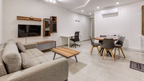 Ein modernes Wohnzimmer mit Sofa, Couchtisch, Fernseher und Essbereich mit Stühlen und einem Tisch.
