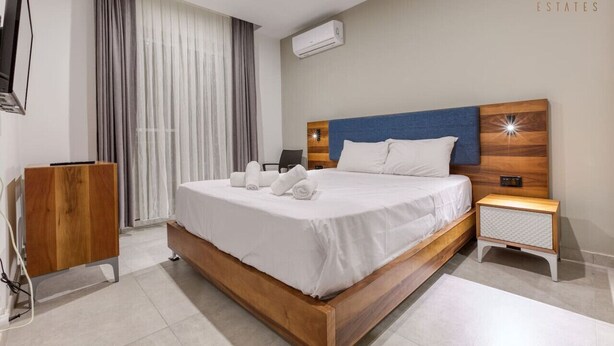 Ein modernes Hotelzimmer mit einem Holzbett, einem Nachttisch, einem Fernseher und einem großen Fenster mit Vorhängen.