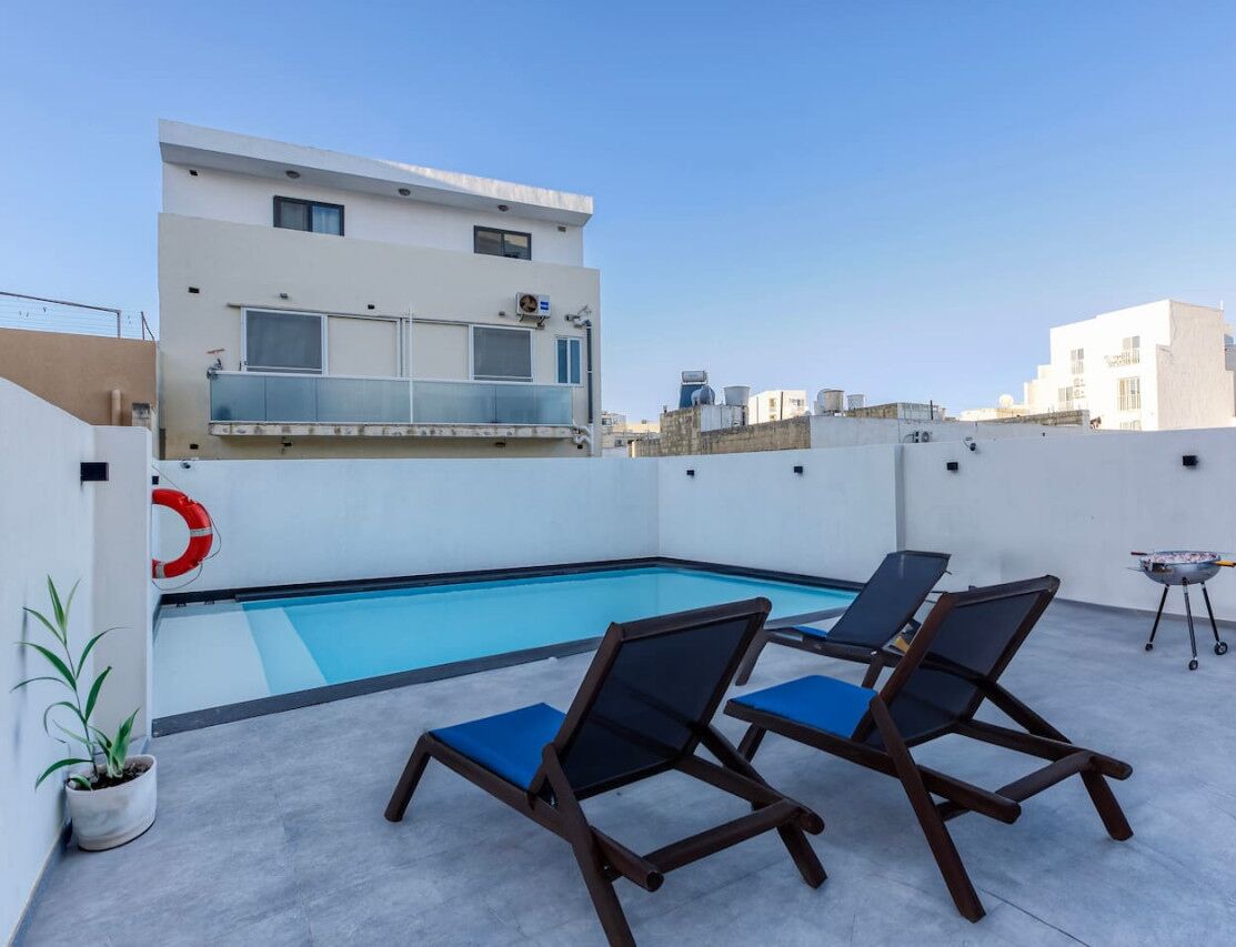 A rooftop pool area with lounge chairs and a barbecue grill.