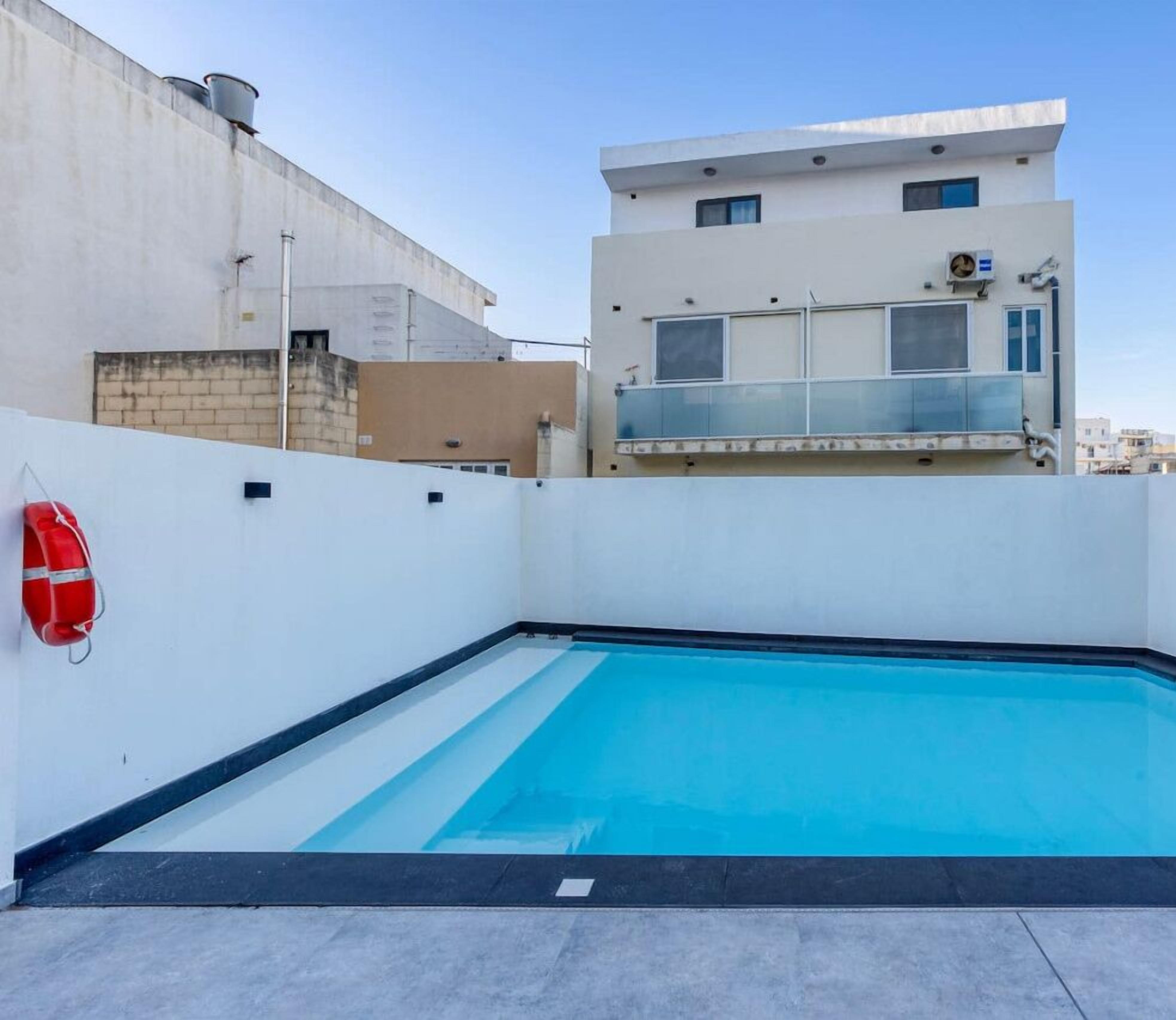 A rooftop swimming pool with a clear blue water surface, surrounded by a white wall and a concrete barrier.