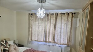 A bedroom with a bed, a radiator, a chandelier, and curtains. - London - Sleeps 4 - Parking - Garden - Petfriendly (London)