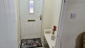 A white door with a small window, a doormat, and a white bench with a vase of dried plants. - London - Sleeps 4 - Parking - Garden - Petfriendly (London)