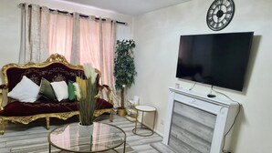 A living room with a red velvet sofa, a glass coffee table, a fireplace, and a flat-screen TV mounted on the wall. - London - Sleeps 4 - Parking - Garden - Petfriendly (London)
