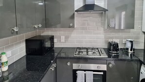 A modern kitchen with grey cabinets, a black countertop, a gas stove, a coffee maker, and a microwave. - London - Sleeps 4 - Parking - Garden - Petfriendly (London)