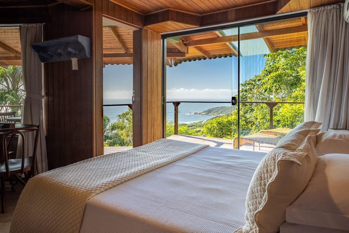 A bedroom with a bed, a desk, and a view of the ocean.