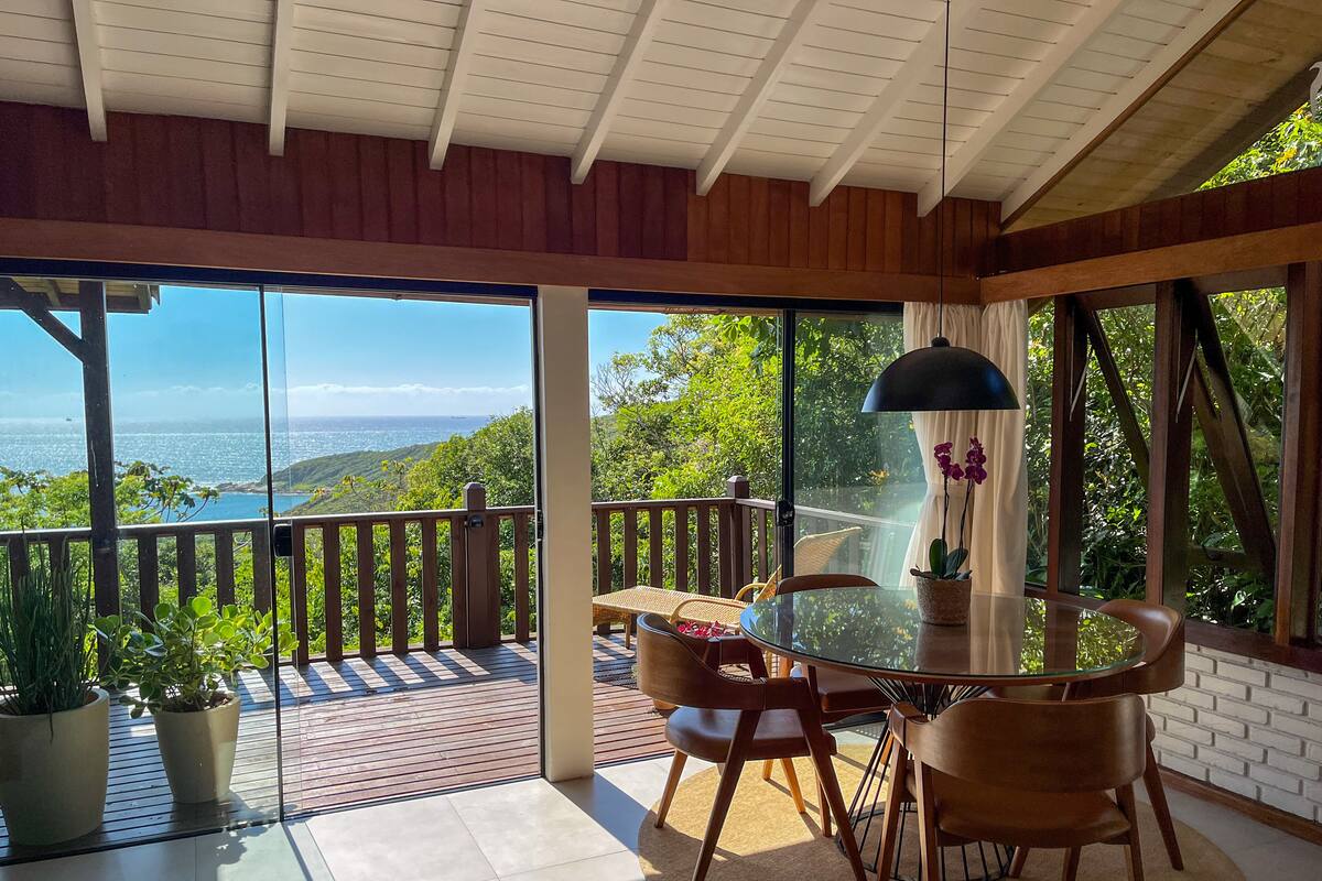 A dining area with a glass table and chairs, a view of the ocean, and a wooden deck.