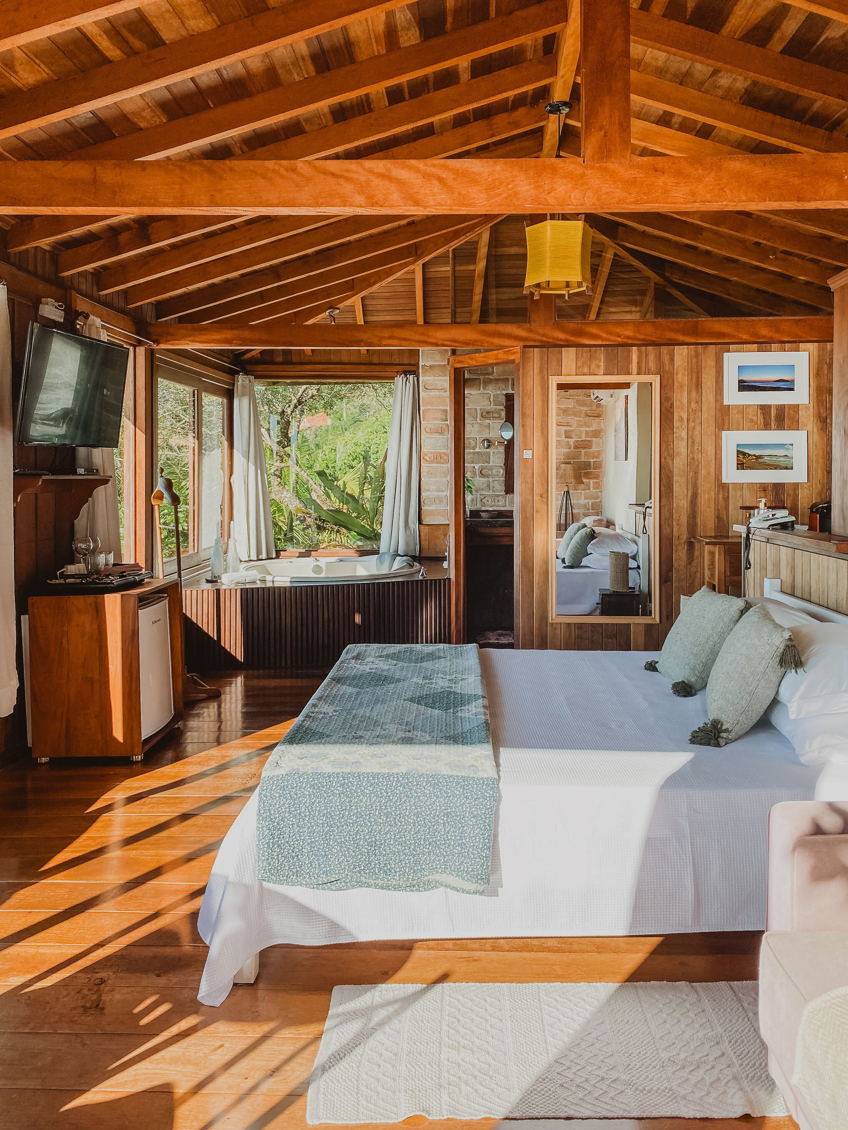 Un dormitorio amplio con una cama grande, vigas de madera en el techo, televisión y vistas al exterior.