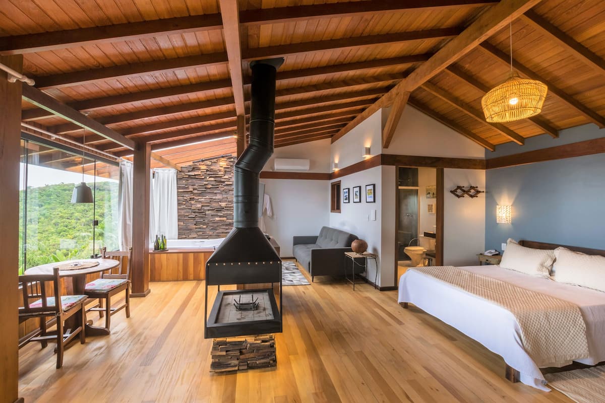 A spacious room with a large fireplace, a bed, a sofa, and a dining area with a view of the outdoors.