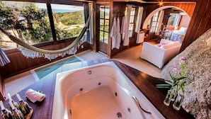 A spa room with a large bathtub, a hammock, and a view of the landscape. - Pousada Caminho do Rei (Imbituba)