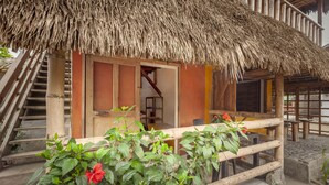 A wooden building with a thatched roof, a staircase, and a small outdoor seating area with a railing. - La Casa Mompiche (Muisne)