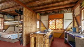 A rustic room with a bunk bed, a wooden table, and a kitchen area with a sink. - La Casa Mompiche (Muisne)