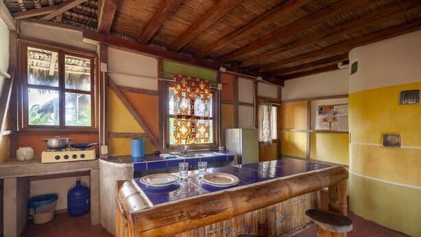A kitchen with a wooden island, a gas stove, a refrigerator, and a window with a decorative curtain. - La Casa Mompiche (Muisne)