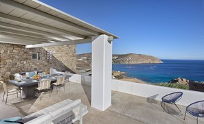 Enjoy meals and conversations in a serene outdoor seating area with ocean views and a distant island.