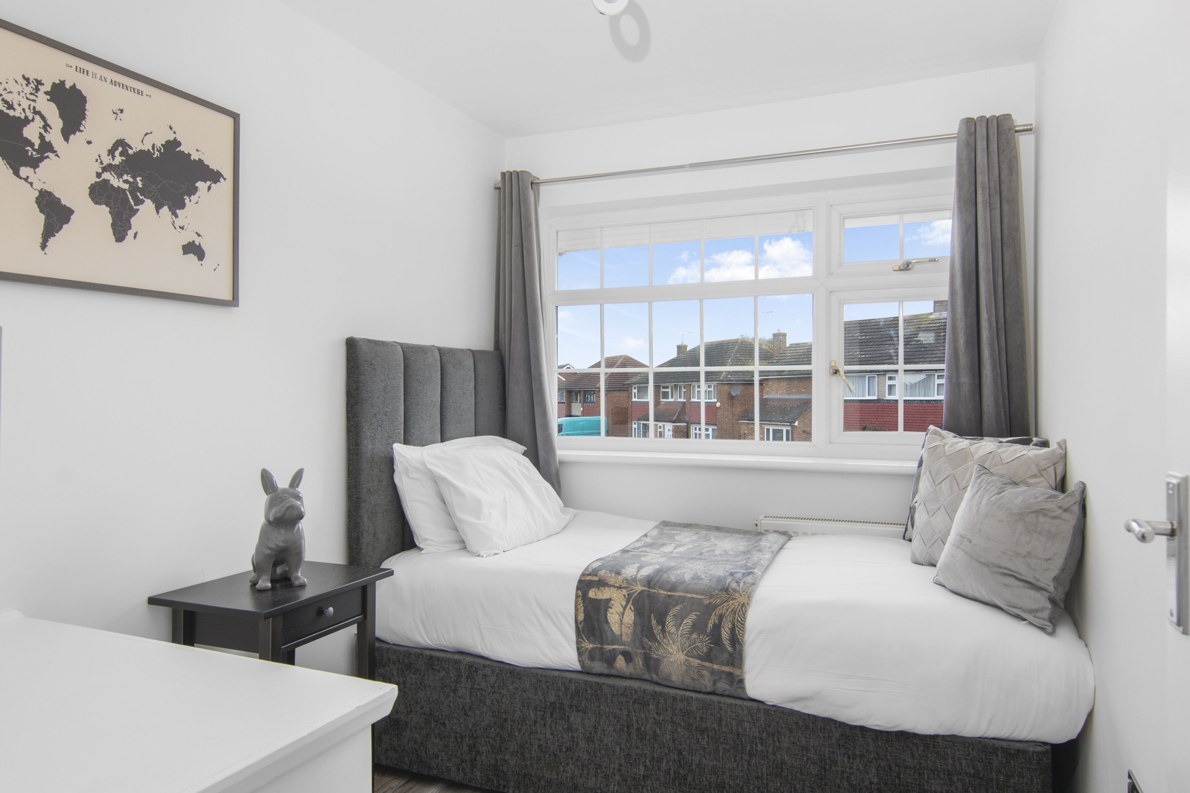 A bedroom with a bed, a nightstand, a world map, and a window with curtains.