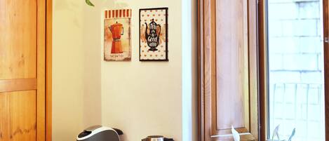 A corner room with a wooden cabinet, a small table with a kettle, cups, and a plant.