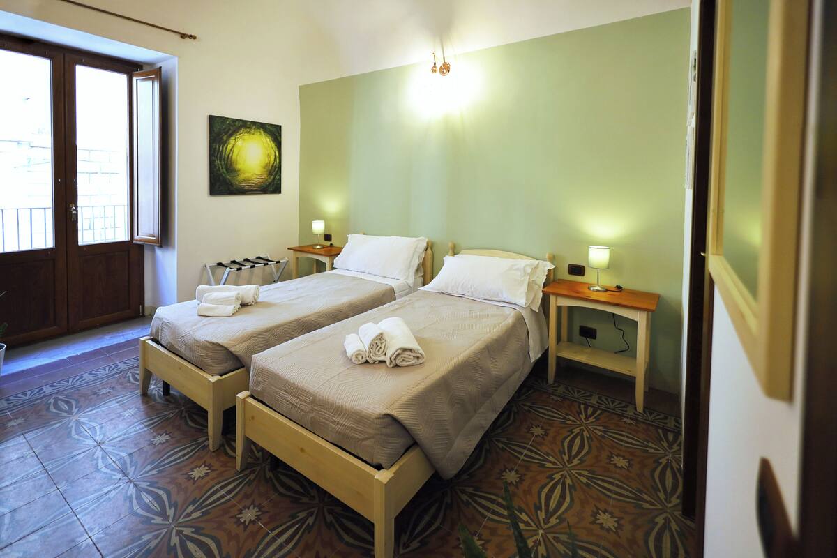 A hotel room with two beds, a wooden bench, a small table, and a wall-mounted artwork.