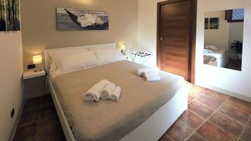 A neatly made bed with rolled towels, a bedside lamp, and a painting on the wall.