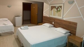 Hotelkamer met twee bedden, een houten hoofdeinde, een klein nachtkastje, een wandlamp en een deur naar een andere kamer.