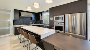 Een moderne keuken met een centraal eiland, roestvrijstalen apparatuur en hanglampen.
