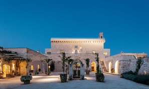 A historic stone building with a central courtyard, arched doorways, and a staircase leading to the upper levels. - Masseria Trapanà (Lecce)