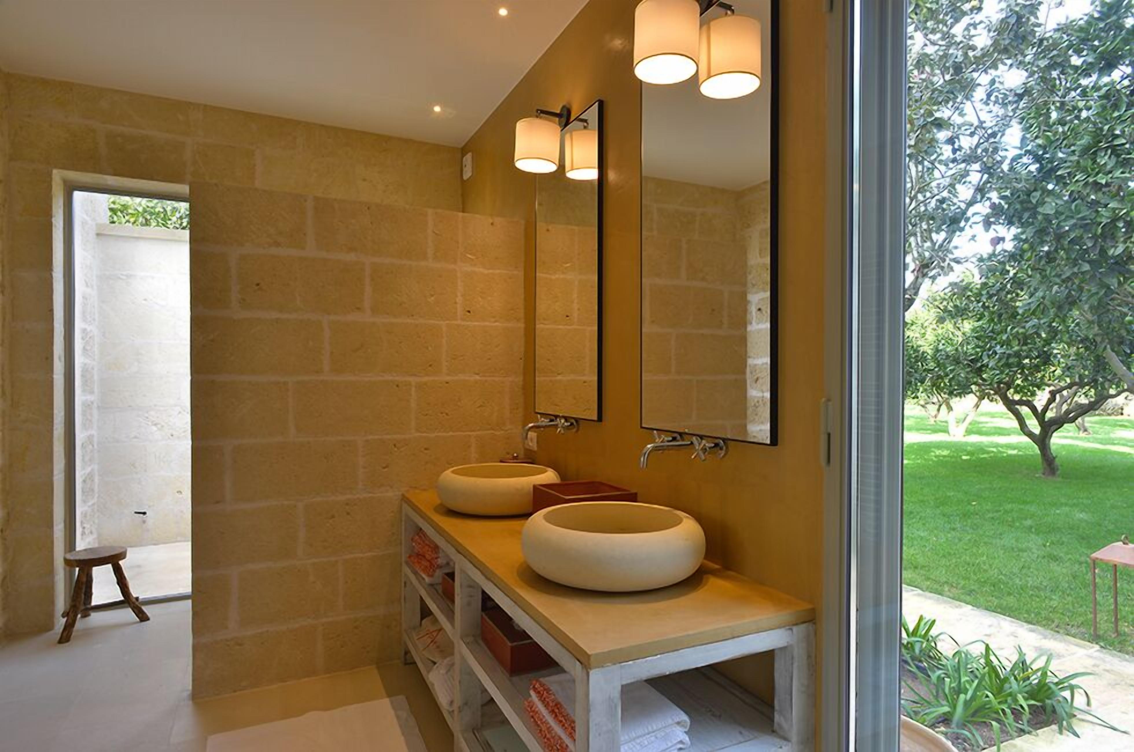 Un baño con dos lavamanos redondos, un espejo grande y una ventana con vista a un jardín.