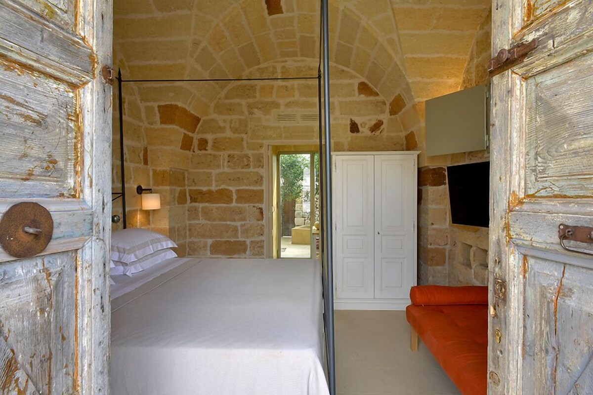 A stone-walled room with a bed, a white wardrobe, and an orange sofa.