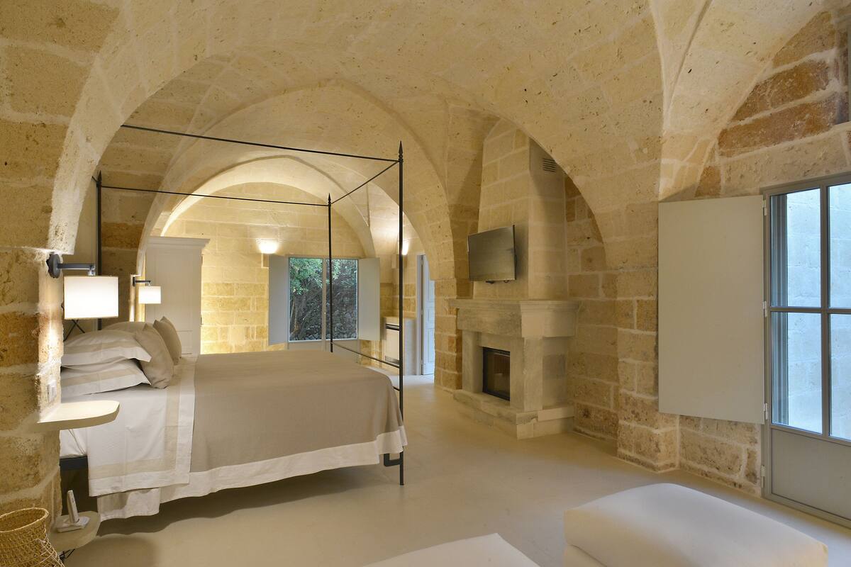 Un dormitorio con techo abovedado de piedra, una cama grande, chimenea y televisor montado en la pared.