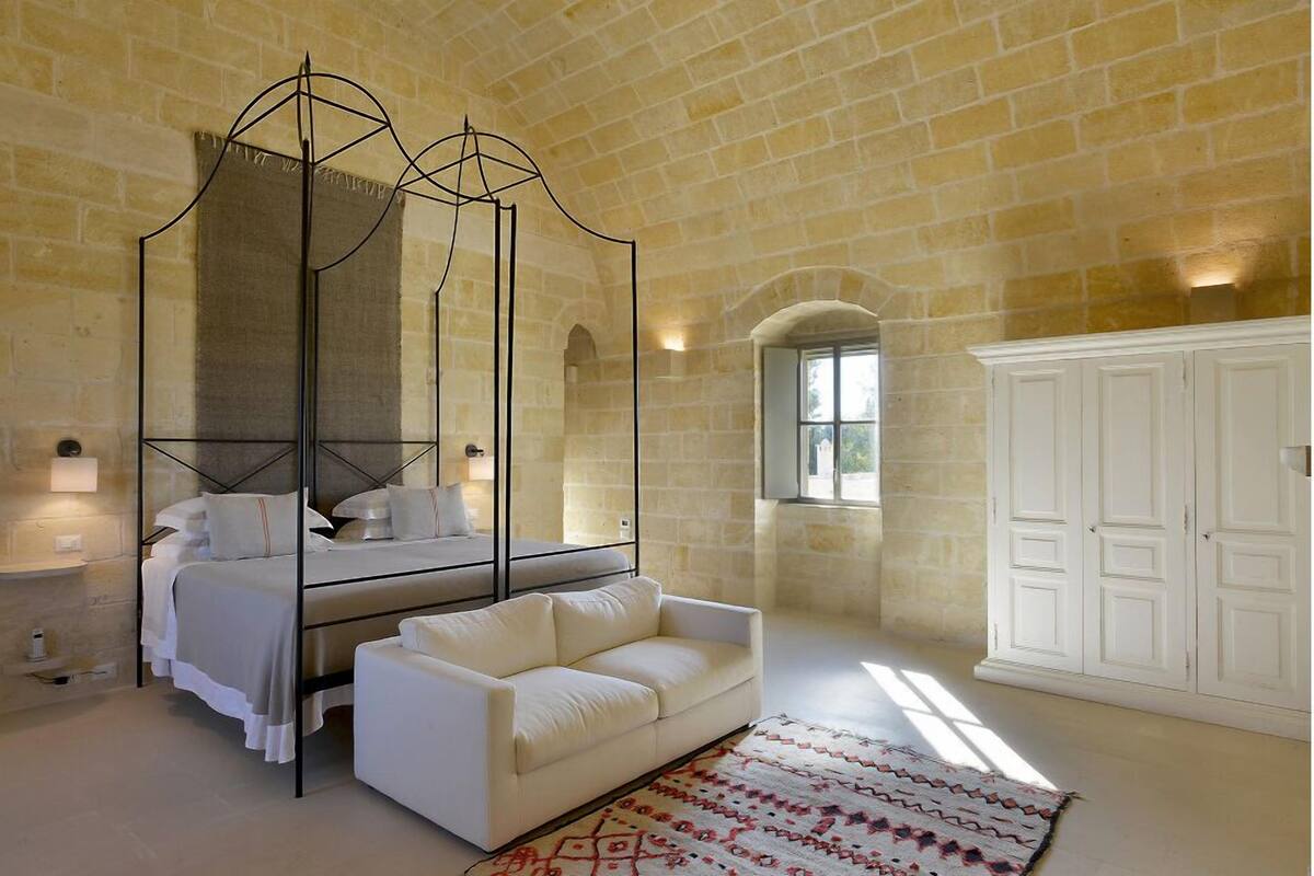 Un dormitorio con cama con dosel, un sofá blanco, un tapete estampado y un armario grande.