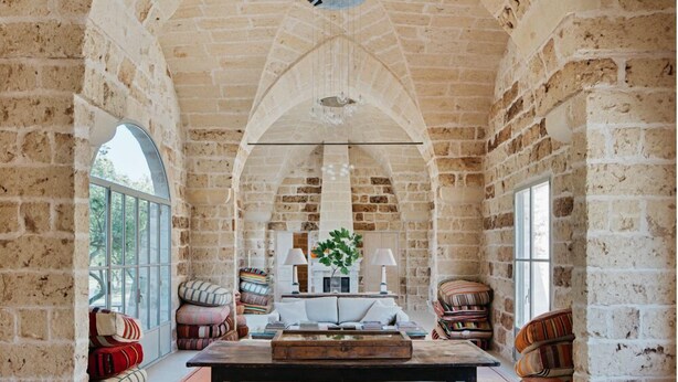 Amplia habitación con paredes de ladrillo visto, un techo abovedado grande y una mesa central con libros y un jarrón.
