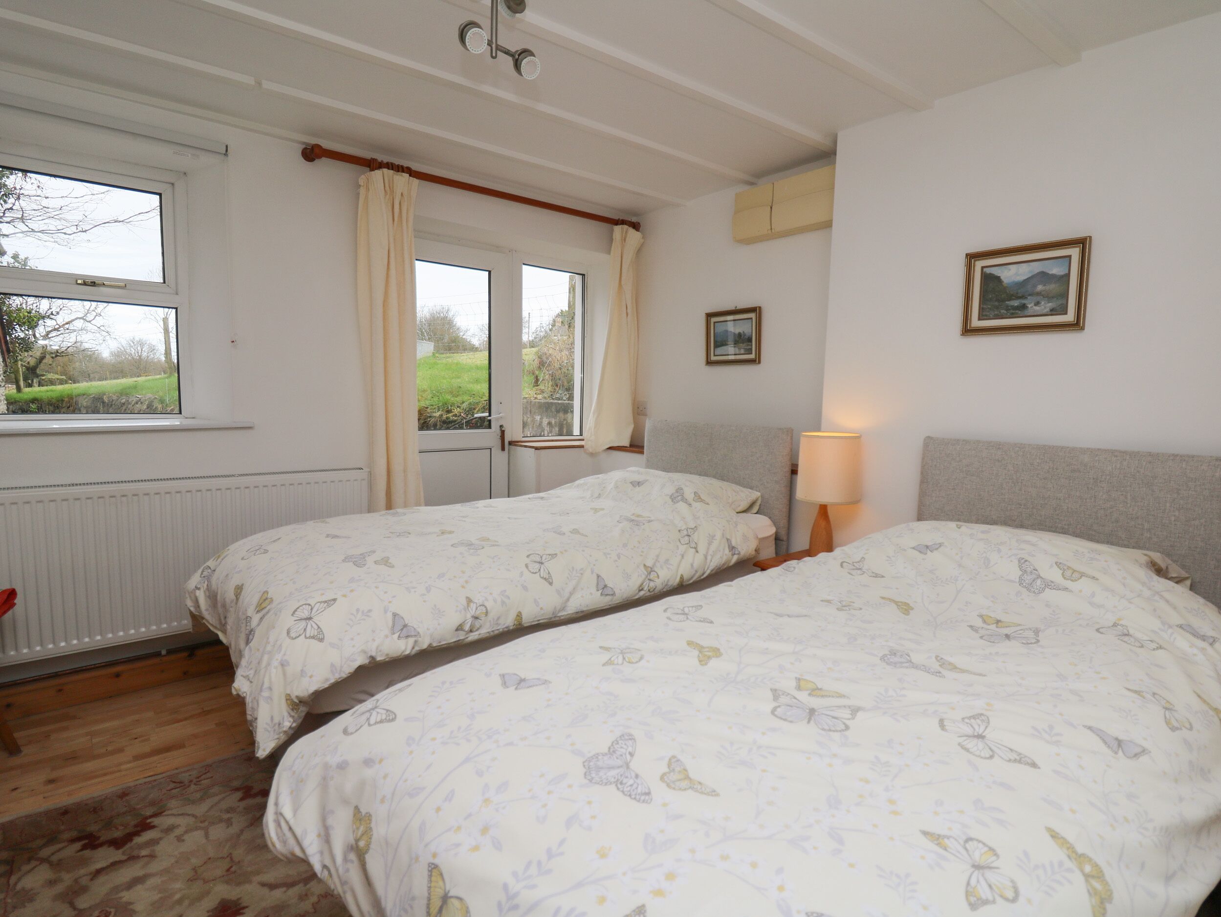 A bedroom with two single beds, a window with curtains, a radiator, and a lamp.