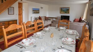 Un coin repas avec une table dressée pour six personnes, des chaises en bois, un canapé et un escalier.