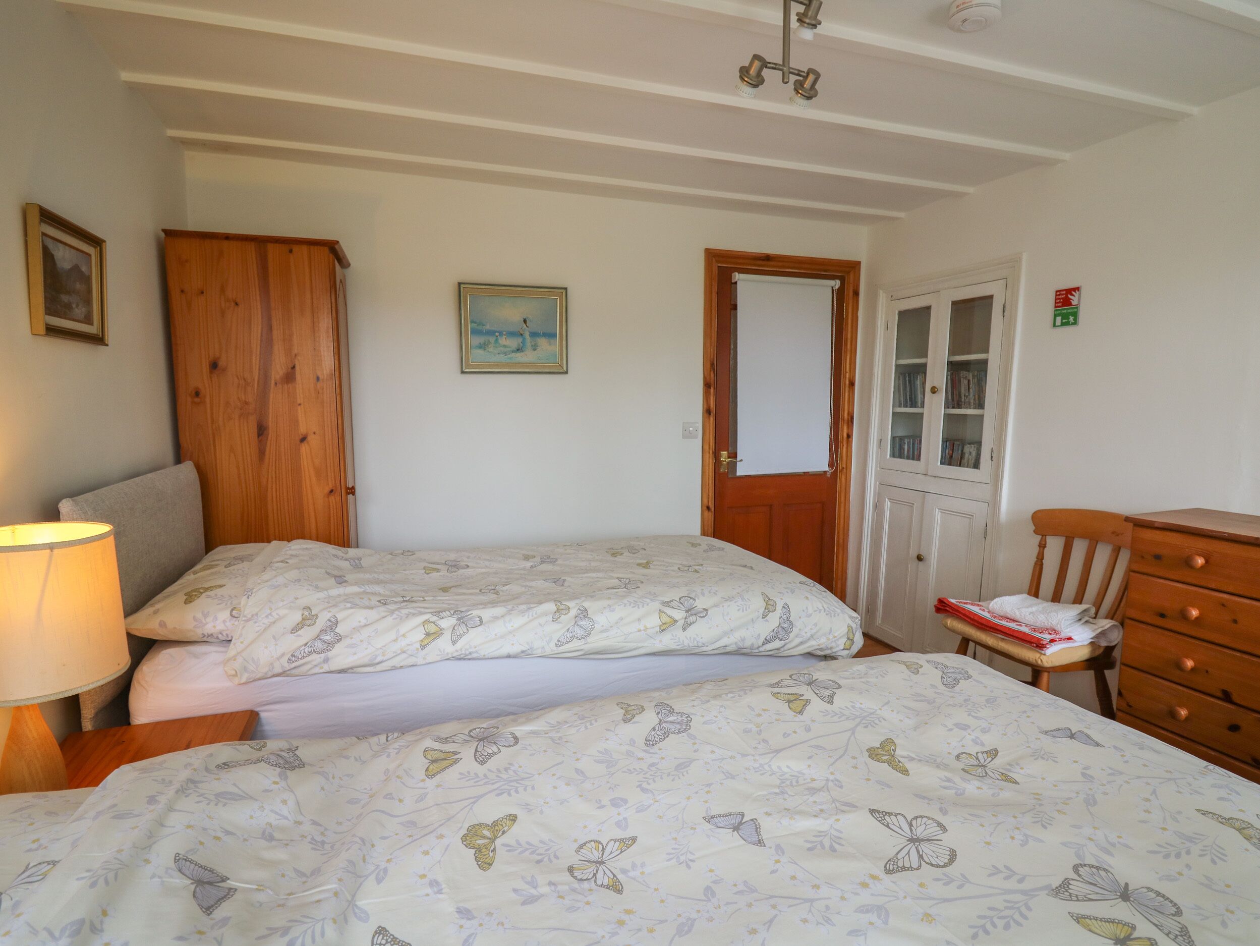 Une chambre avec deux lits, une armoire en bois, une petite table avec une chaise et un meuble contenant des livres.