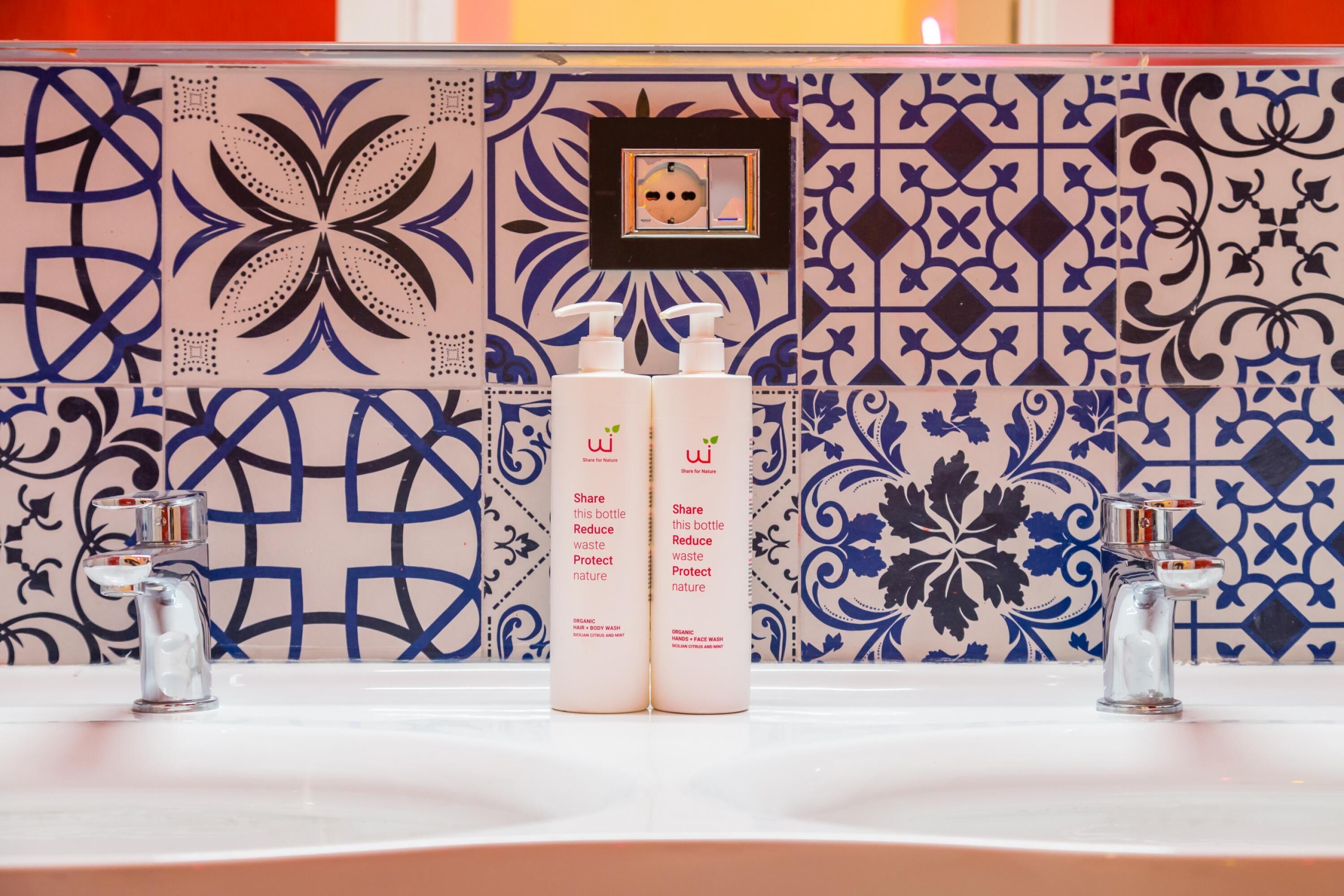 Une salle de bain avec des carreaux décorés, deux lavabos et deux flacons de savon pour les mains.