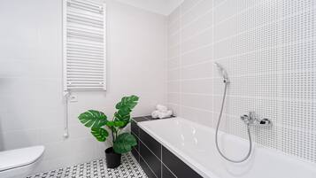 Une salle de bain moderne avec une baignoire blanche, des carreaux de sol à motifs noirs et blancs, une plante en pot et des toilettes blanches.