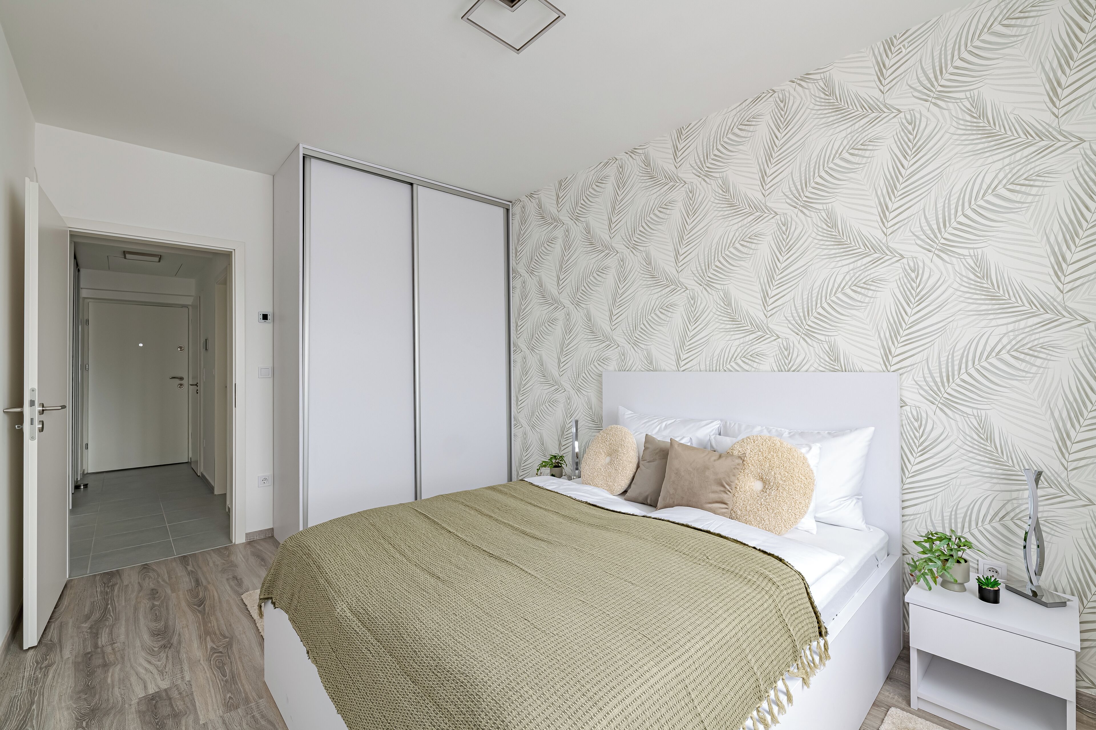 Ein Schlafzimmer mit einem Bett, einem Nachttisch, einer Wand mit Blattmuster und einer Tür zu einem anderen Raum.