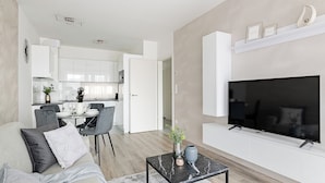 Una sala de estar moderna con un televisor de pantalla plana, un sofá, una mesa de centro y una zona de comedor al fondo.