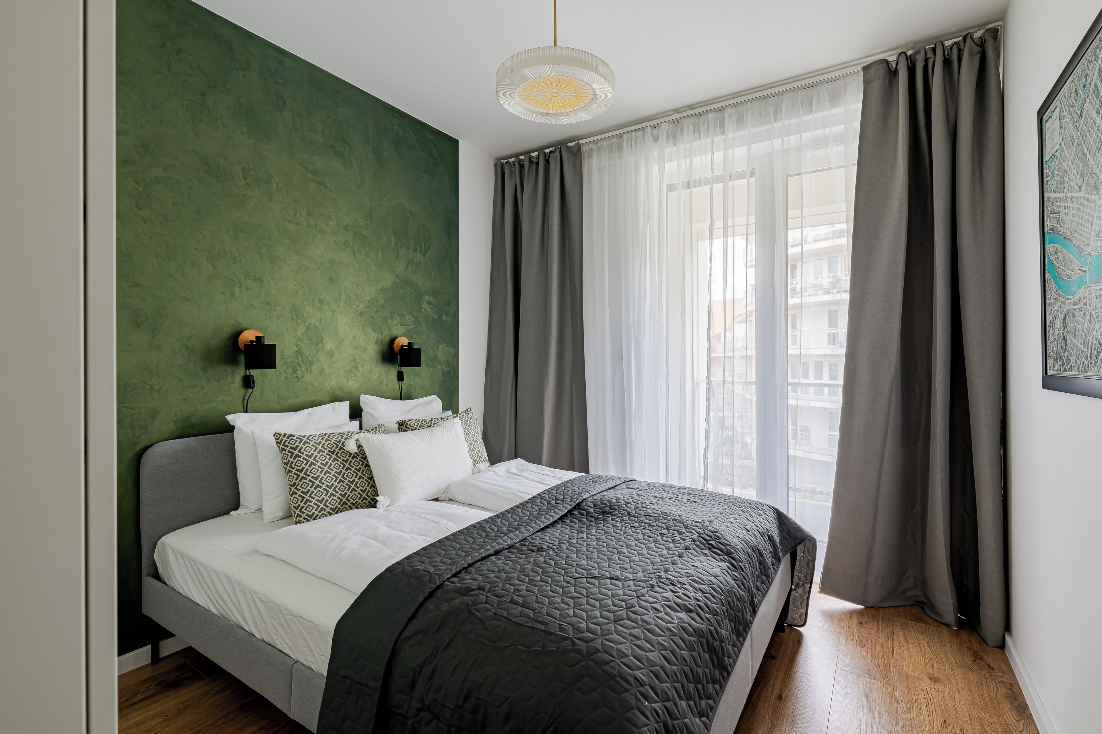 Un dormitorio moderno con una pared de acento verde, una cama gris y un gran ventanal con cortinas grises.