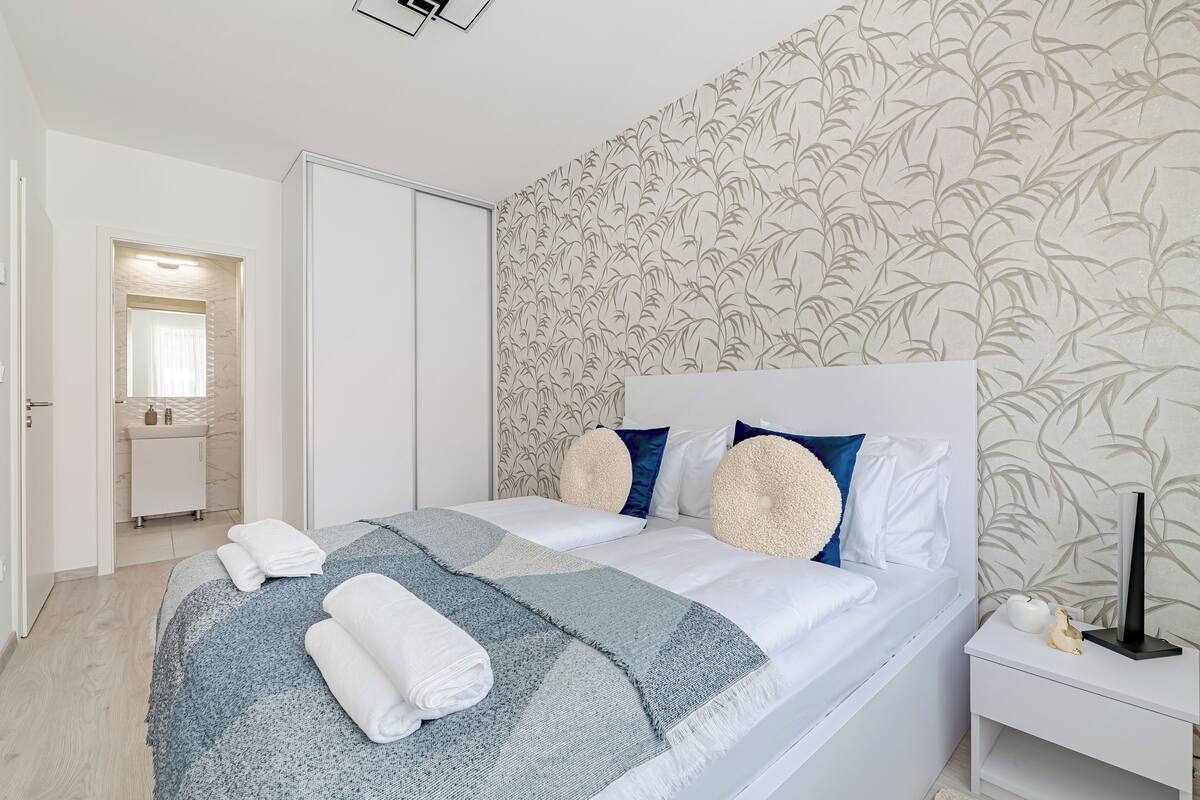 Ein modernes Schlafzimmer mit einem großen Bett, einem Nachttisch mit Lampe und einem durchgegangene Tür einsehbaren Badezimmer.