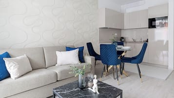 A modern living room with a sofa, blue chairs, a marble coffee table, and a kitchen in the background.